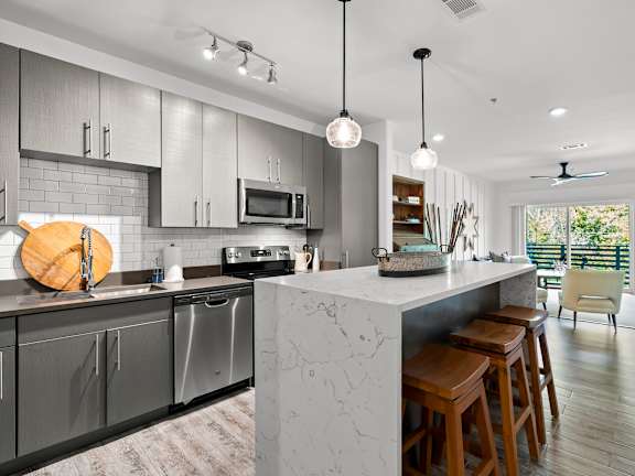 A modern kitchen with a marble island and wooden stools.