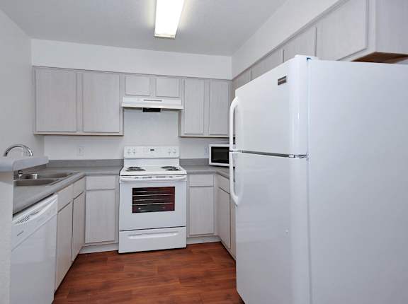 A white refrigerator stands in a kitchen with wooden floors and white cabinets.