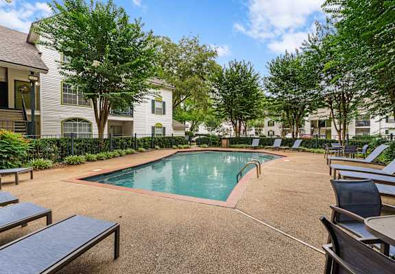 A pool surrounded by trees and chairs.