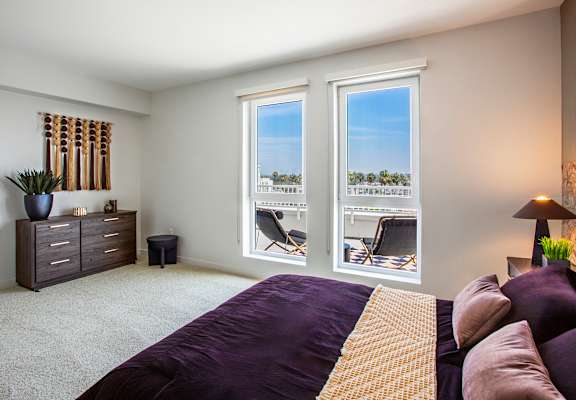 A bedroom with a bed, dresser, and window with a view of a parking lot.