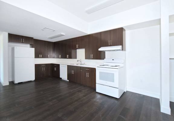 an empty kitchen with white appliances and wood floors