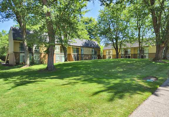a grassy area with trees in front of an apartment building