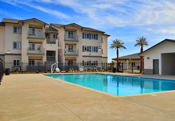 A swimming pool in front of a building with a fence and palm trees.