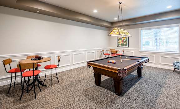 A pool table is in the middle of a room with chairs and a table.