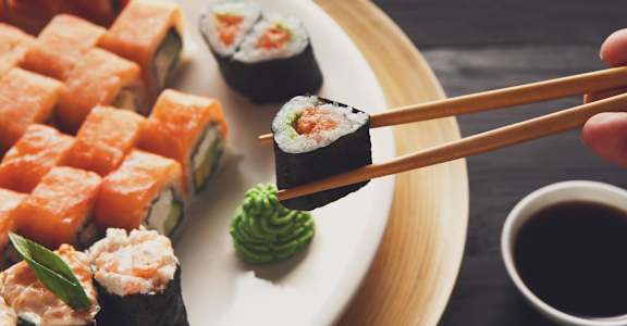 a plate of sushi with a person holding a chopstick with a piece of sushi on it at Aston at Gateway Apartments, El Monte, California