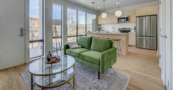 A modern kitchen with a green couch and a glass table.