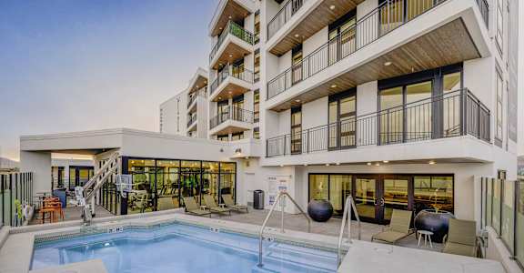 A large swimming pool is surrounded by a patio area with chairs and a hot tub.