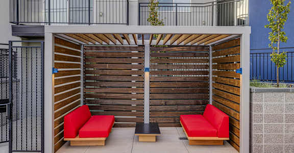 A wooden bench with red cushions is in front of a wooden fence.