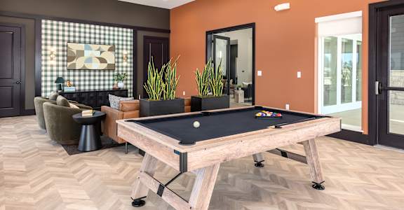 A pool table is in the middle of a room with a brown floor and orange walls at Montage at Hawk Ridge Apartments, Lake St. Louis, MO