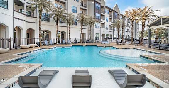 A swimming pool surrounded by lounge chairs and palm trees in front of a building at The Addison,Louisiana 70836