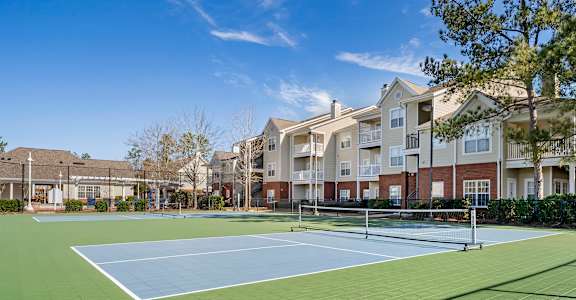 A tennis court is surrounded by apartment buildings.