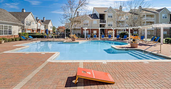 A pool surrounded by a brick patio with a bench in the foreground.