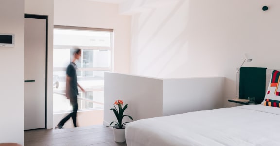 a room with a bed and a person walking out of a window