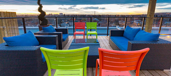 A balcony with a view of the city at dusk, furnished with blue cushions and colorful chairs.