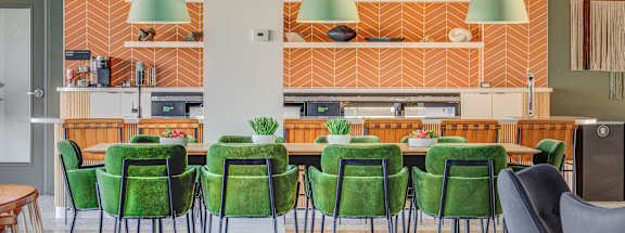 a large table with green chairs and a kitchen in the background