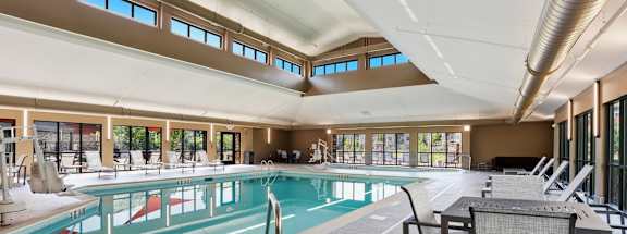 A large indoor swimming pool with lounge chairs and a metal pole.