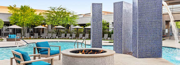 A poolside area with a fire pit, chairs, and umbrellas.