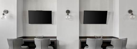 Two chairs are placed in front of two TVs on a wall.