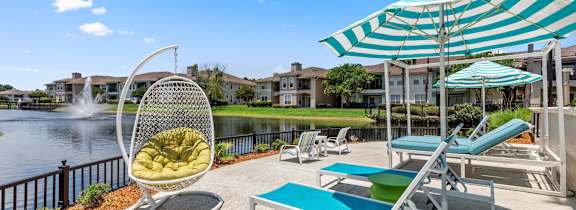 A sunny day at the poolside with a chair, table, and umbrella.