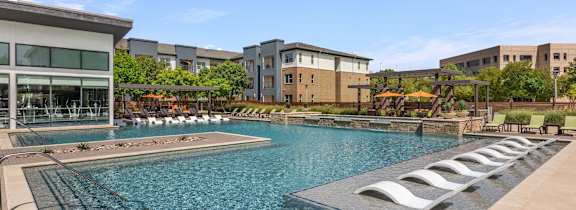 A large swimming pool with lounge chairs is surrounded by buildings.