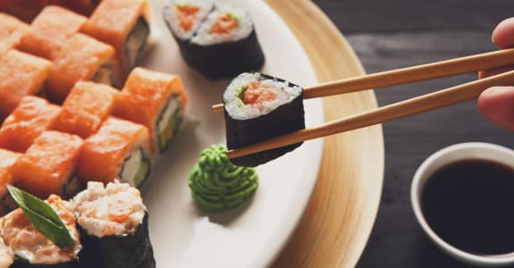 a plate of sushi with a person holding a chopstick with a piece of sushi on it