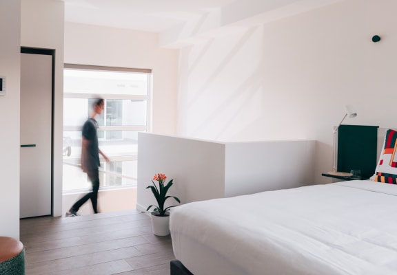 a room with a bed and a person walking out of a window