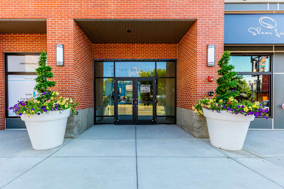The front of a building with a glass door and two large planters with flowers.