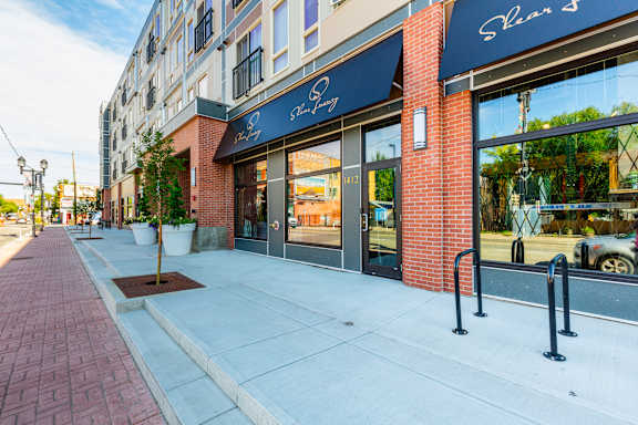 A brick sidewalk leads to a storefront with a blue awning.