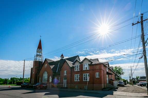 A church with a steeple and a cross on top is surrounded by power lines and has a clear blue sky above it.