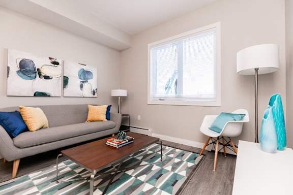 A living room with a grey couch, a coffee table, a chair, and a painting on the wall.