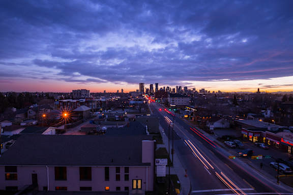 A cityscape at dusk with buildings and a long exposure of the street lights.