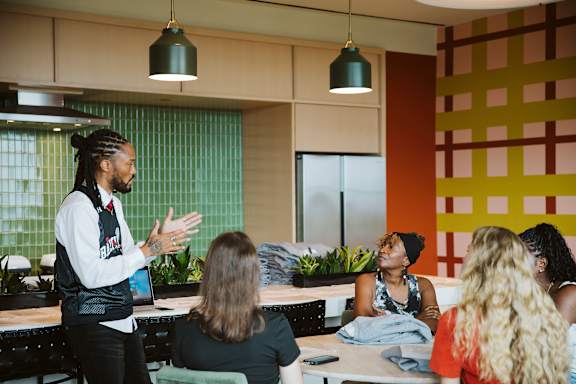 A man in a black vest is talking to a group of people in a room with a green wall at Scout Living, powered by Placemakr, Atlanta, 30308