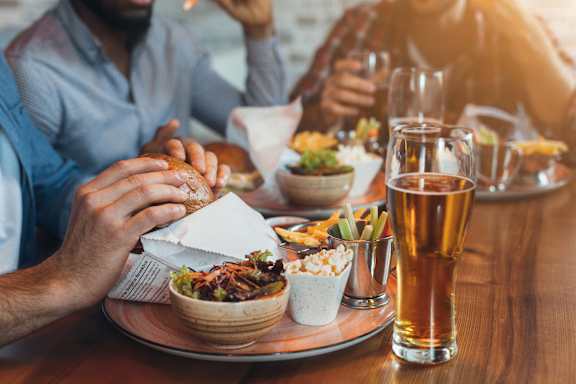 A person is eating a burger with a side of salad and a glass of beer.