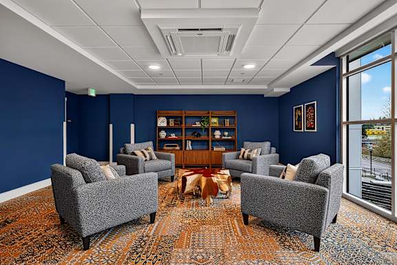 A room with blue walls and a carpeted floor with a wooden bookshelf and grey chairs.