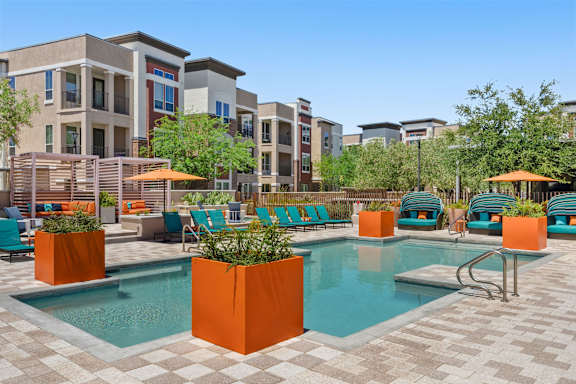 A pool surrounded by orange planters and chairs.