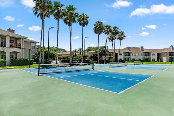 A tennis court surrounded by palm trees and apartment buildings.