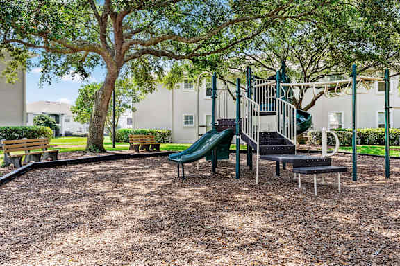 A playground with a green slide and a tree.