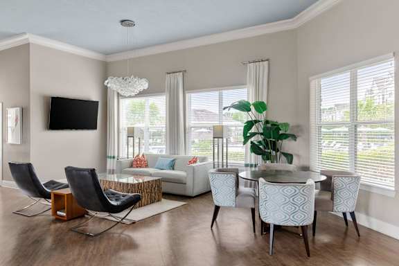 A modern living room with a white sofa, a glass coffee table, and a TV mounted on the wall.