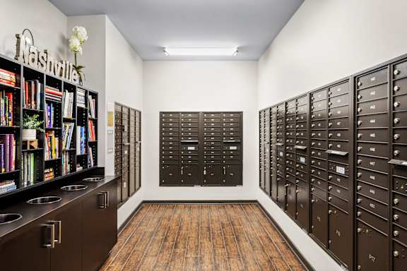 A room with a bookshelf, mailboxes and a vase of flowers.