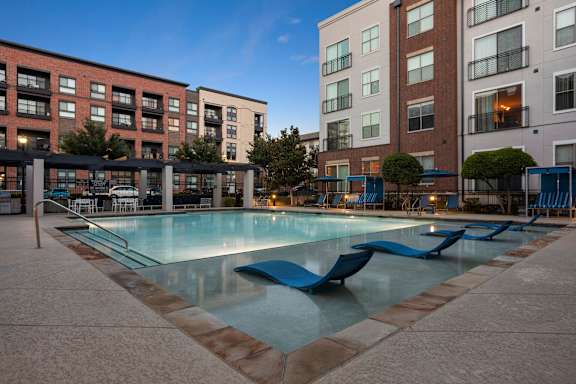A swimming pool surrounded by a poolside lounge area and apartment buildings.