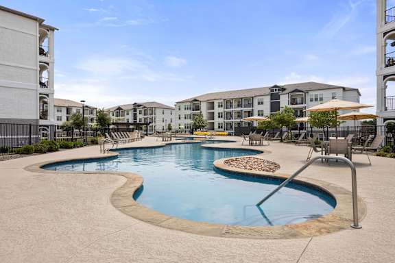 A large outdoor swimming pool surrounded by a concrete patio and chairs.
