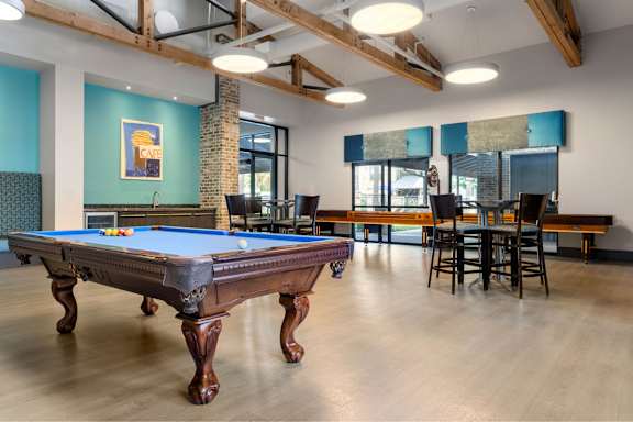 A pool table is in the middle of a room with a brick pillar and a bar area.