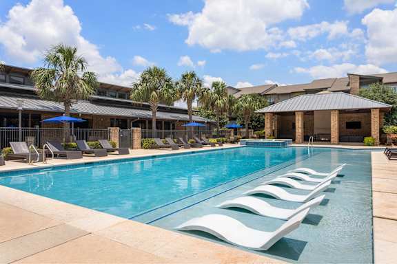 A pool with sun loungers and a building in the background.
