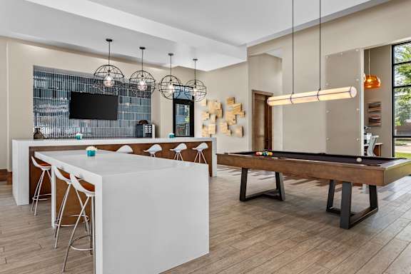 A billiard table is in the middle of a room with a bar and a television.