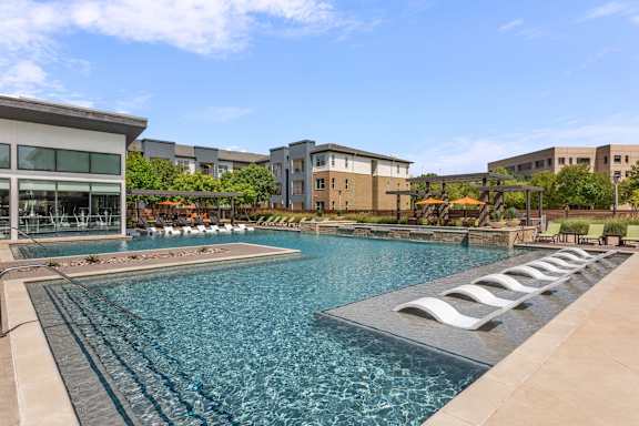 A large swimming pool with lounge chairs is surrounded by buildings.