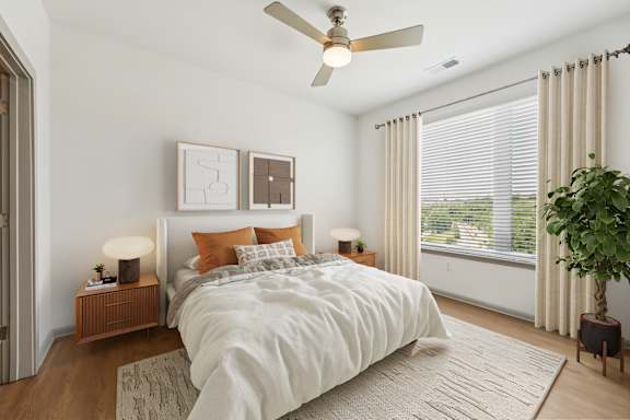 A bedroom with a large bed, a ceiling fan, and a potted plant.