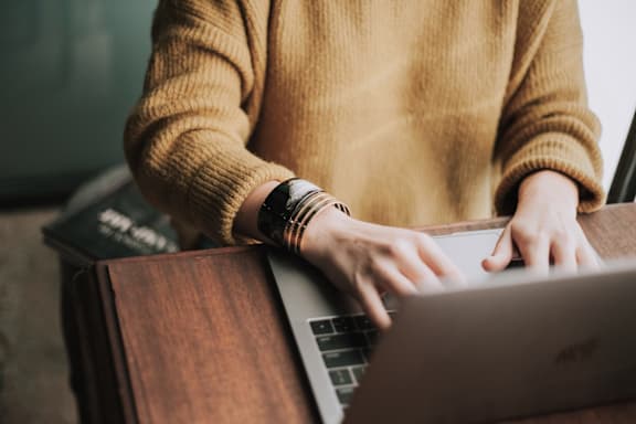 A person in a yellow sweater is typing on a laptop. at Vintage Edge Nashville Apartments, Tennessee, 37211