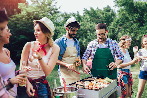 A group of people are gathered around a barbecue grill in a park.