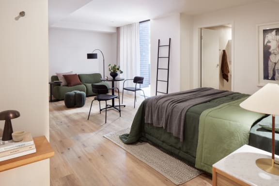 a bedroom with a green bed and a living room with a table and chairs