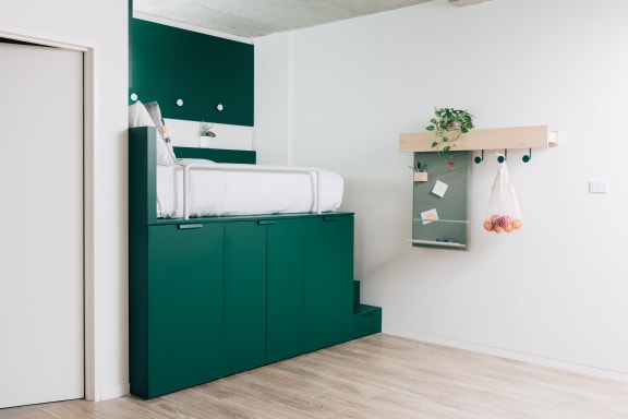 a green cabinet with a white bed in a room with a door